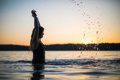 Beautiful girl in a long black swimsuit swims on the lake in the rays of sunset or dawn