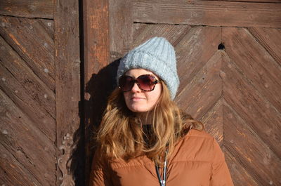 Woman wearing sunglasses while standing against wooden door