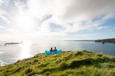 Young couple sits in air sofa on coastline enjoying the beautiful scenic view of sea against sky.