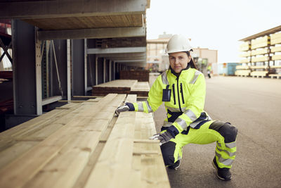 Portrait of female worker in protective workwear stacking planks at lumber industry