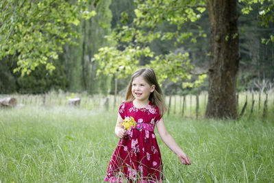 Young girl walking through long green grass holding yellow flowers