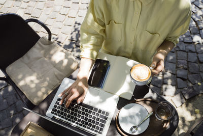 Freelancer with coffee cup working on laptop sitting at sidewalk cafe