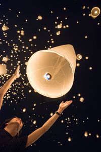 Low angle view of man with arms raised looking at illuminated lanterns at night