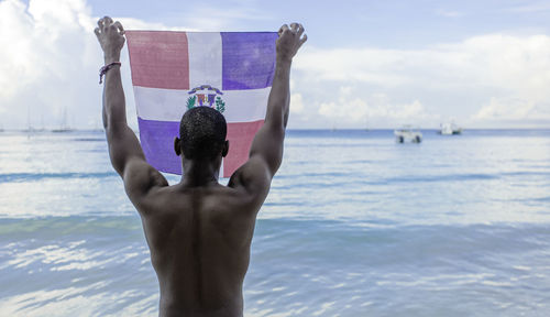 African american male from behind raising the flag of dominican republic on the beach summer weekend