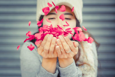 Close-up of woman blowing heart shape petals on cupped hands