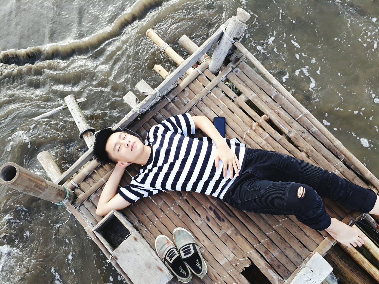 high angle view, lying on back, water, real people, lying down, leisure activity, one person, day, nautical vessel, looking at camera, full length, outdoors, relaxation, wood - material, casual clothing, young adult, young women, lake, transportation, directly above, portrait, lifestyles, wooden raft, raft, vacations, hands behind head, boat deck, beautiful woman, people