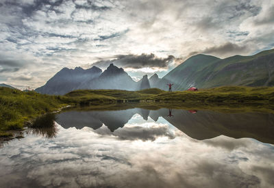 Mid distance view of woman standing at lakeshore against mountains