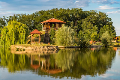 House by lake and trees against sky