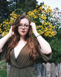 Portrait of beautiful young woman standing against flowering plants