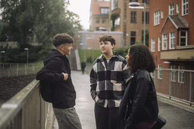 Side view of teenage boy talking with male and female friends standing at footpath