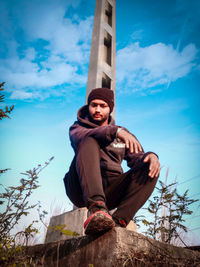 Low angle view of young man sitting against sky
