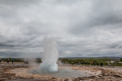 People by geyser against cloudy sky