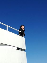 Low angle view of young woman standing on terrace against clear blue sky