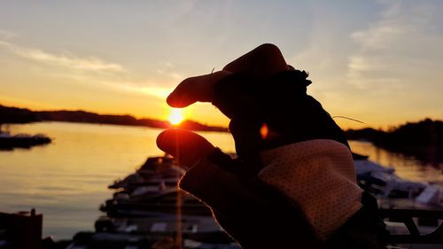 Close-up of silhouette hand on beach against sky during sunset