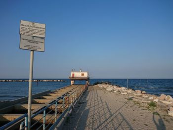 Information sign on beach against clear sky