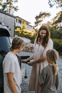 Mother charging electric car and talking with sons standing on driveway