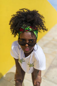 Portrait of young woman standing against yellow wall and sky