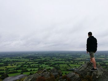 Rear view full length of man on cliff looking at landscape against sky