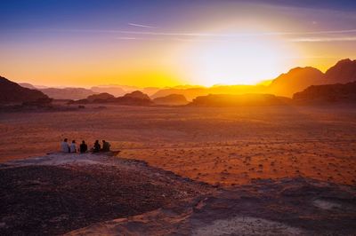 Rear view of friends sitting on rock at wadi rum during sunset