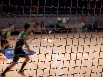 Running players in sport hall. view through the protective net of a floorball match.