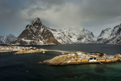 Aerial view of snowcapped mountains by sea against sky