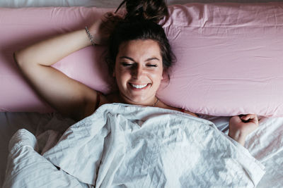 High angle view of smiling young woman lying on bed