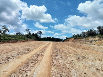 Dirt road amidst field against sky