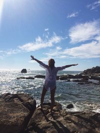 Rear view of woman with arms outstretched standing on rocky shore