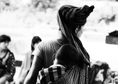 Rear view of mother carrying daughter in baby sling