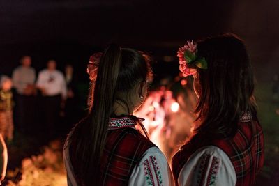 Rear view of friends in traditional clothing by campfire at night