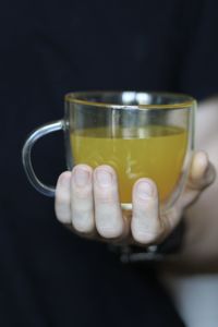 Close-up of hand holding tea cup against black background