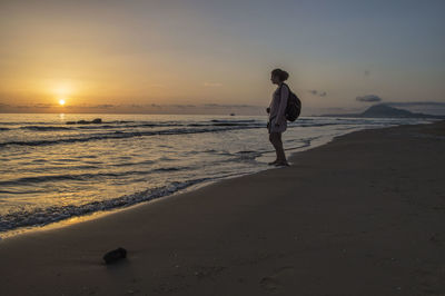 Side view full length of woman standing at beach during sunset