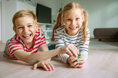 Portrait cheerful siblings playing with dice while lying on carpet at home