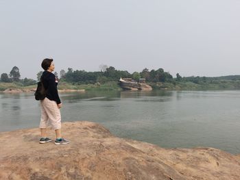 Rear view of man standing on shore against clear sky