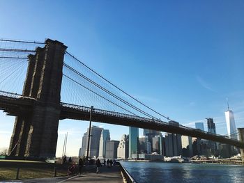 Low angle view of brooklyn bridge over east river in city against blue sky