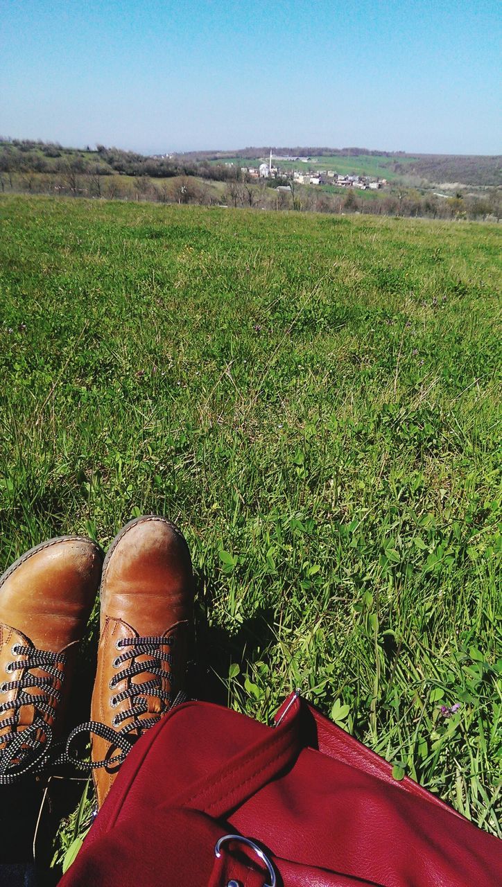 grass, field, low section, landscape, clear sky, person, shoe, personal perspective, grassy, relaxation, nature, growth, tranquility, sunlight, green color, tranquil scene, footwear