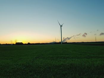 Wind turbines on grassy field at sunset