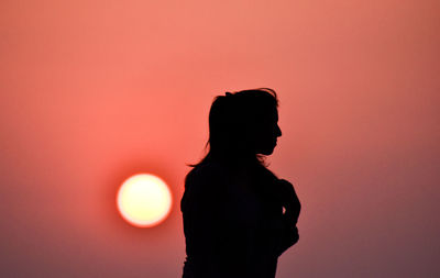 Silhouette woman standing against orange sun