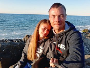 Portrait of smiling couple sitting by sea against sky