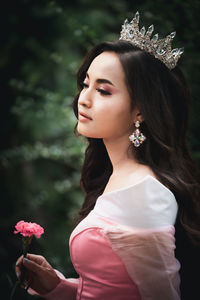 Close-up of smiling woman wearing crown holding flower standing outdoors