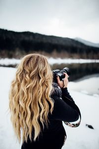 Woman photographing while standing on snow covered land