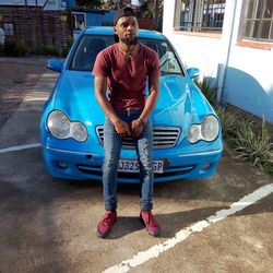 Full length portrait of young man sitting on car