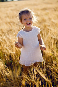 Little girl is happy on the field with ears in the evening sunset in summer.