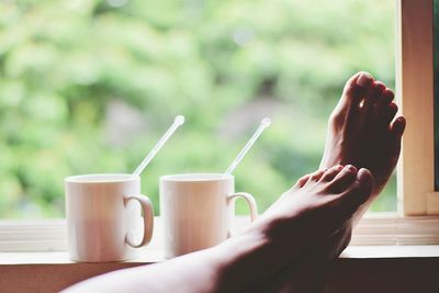 Low section of woman by cups on window sill at home