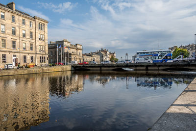 Bridge over river by buildings against sky in city