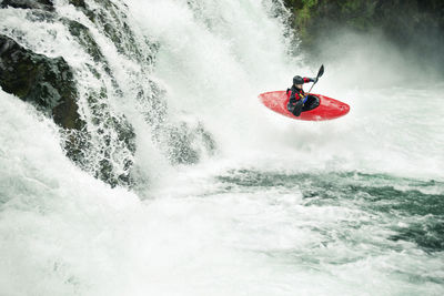 Whitewater kayaker paddling through river in forest