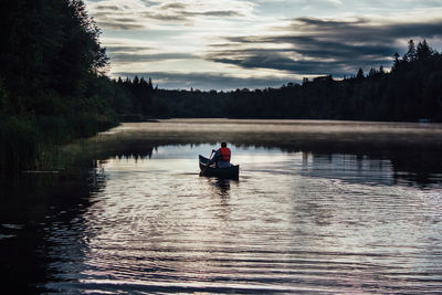 Man sitting in boat on lake against sky