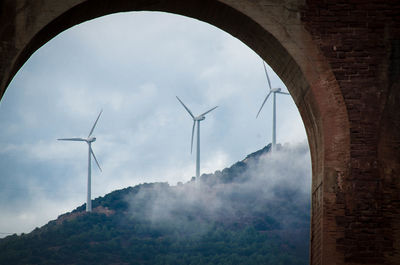 Low angle view of windmill and mountains against sky