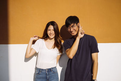 Portrait of a smiling young woman standing against wall