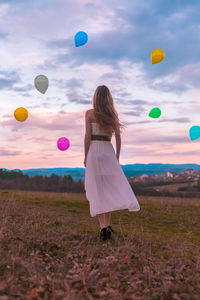 Rear view of woman with balloons in field against sky